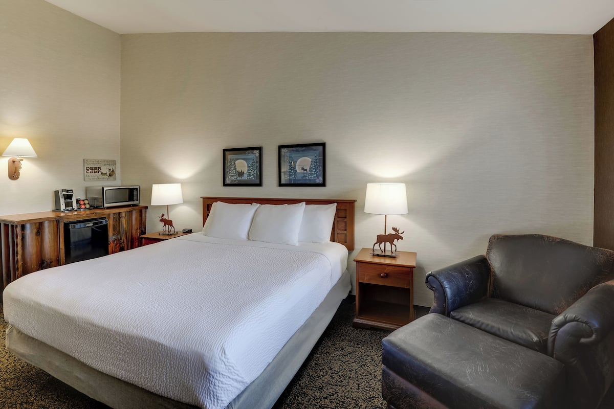 A hotel room with a large bed, two bedside tables with lamps, a desk with a telephone and a coffee maker, and a leather armchair.