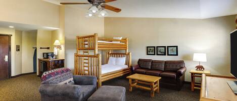 A hotel room with a bunk bed, a sofa, a coffee table, a TV, and a ceiling fan.