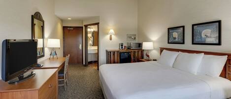 A hotel room with a large bed, a TV on a wooden dresser, a desk with a lamp, and a microwave.