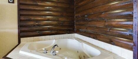 Un baño con una bañera grande, paredes de paneles de madera y suelo de baldosas.