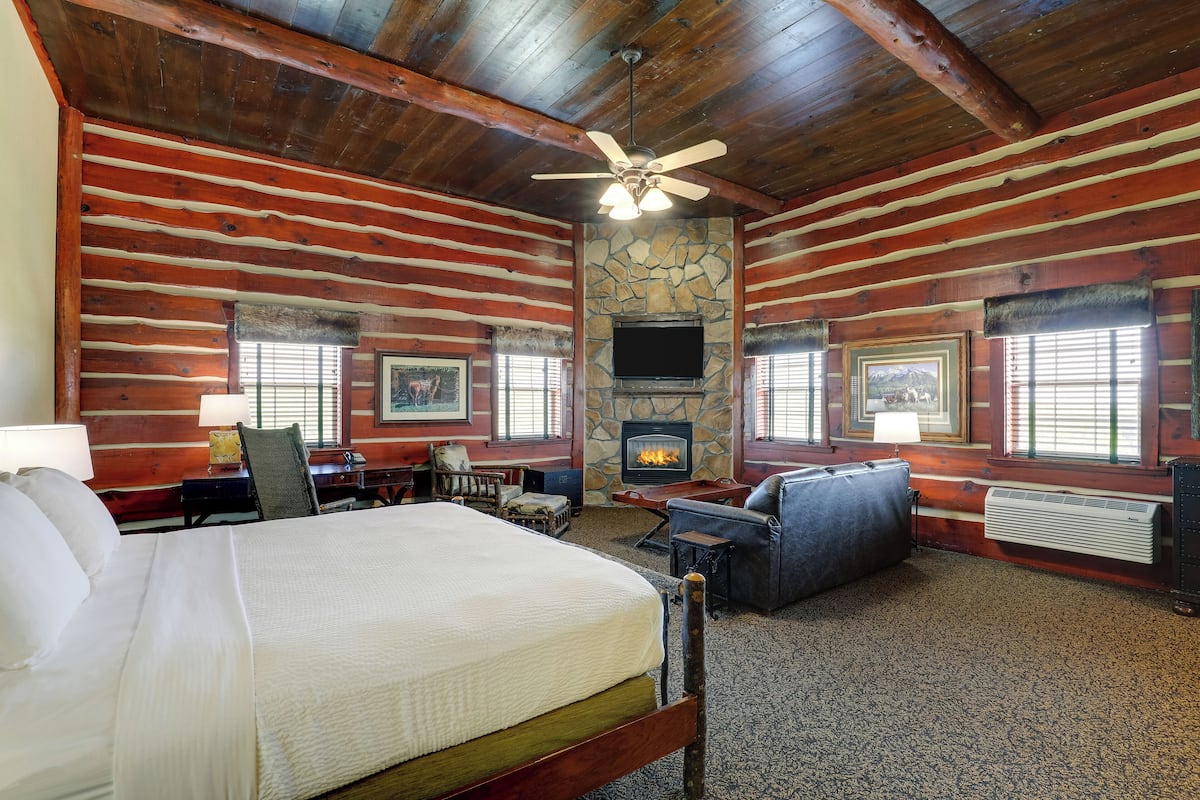 A log cabin-style room with a bed, a fireplace, a television, and a stone wall.