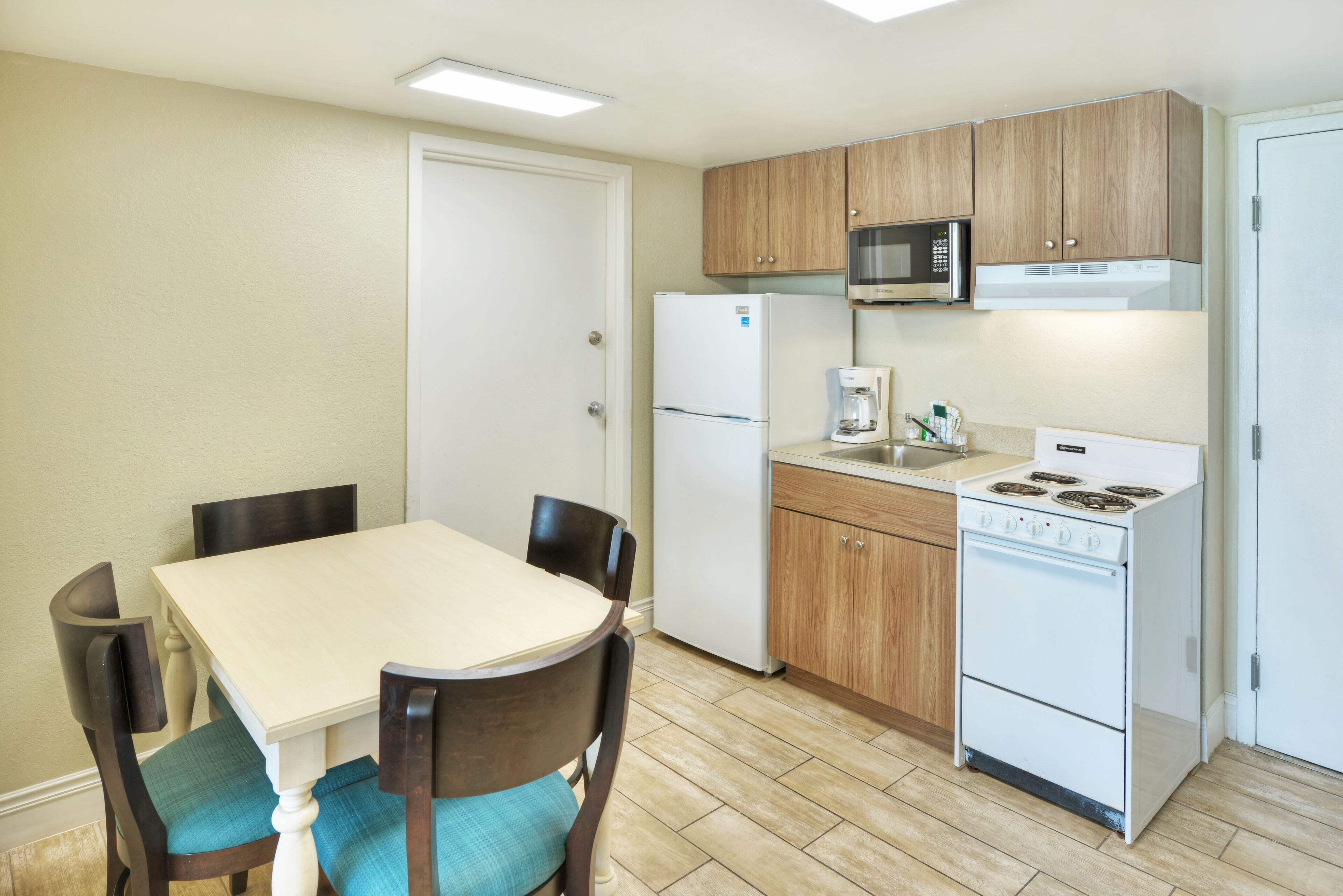 A compact kitchen with wooden cabinets, a white refrigerator, a microwave, a coffee maker, and a stove.