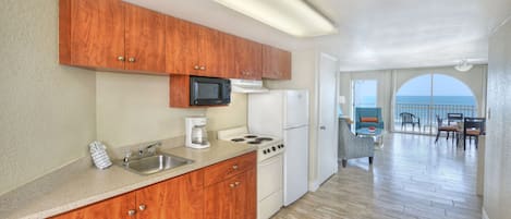 A kitchen with wooden cabinets, a microwave, stove, and refrigerator. There is a dining area with a view of the ocean.
