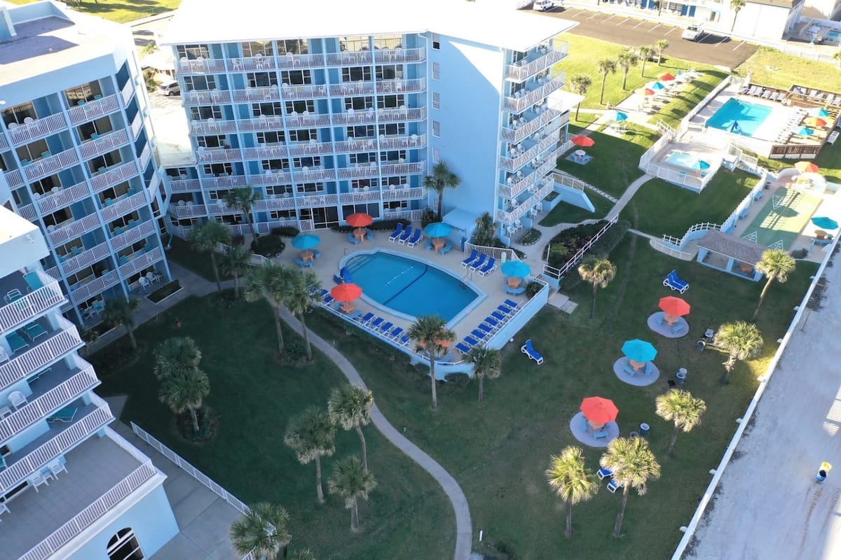Ein mehrstöckiges Hotel mit einem zentral gelegenen Schwimmbad, umgeben von Liegestühlen und Sonnenschirmen.