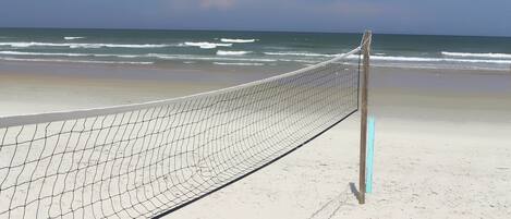 Una red de voleibol de playa en una arena con el océano al fondo.