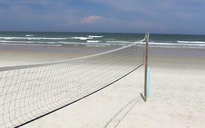 Un filet de volley-ball sur une plage de sable, avec l’océan en arrière-plan.