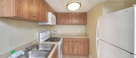 A compact kitchen with wooden cabinets, a stainless steel sink, a white refrigerator, and a built-in microwave.