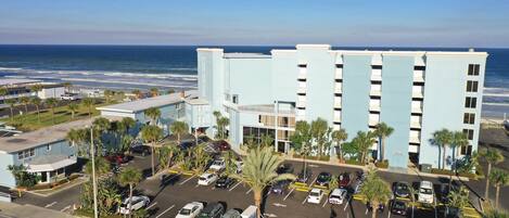 A multi-story hotel with a parking lot, palm trees, and a view of the ocean.