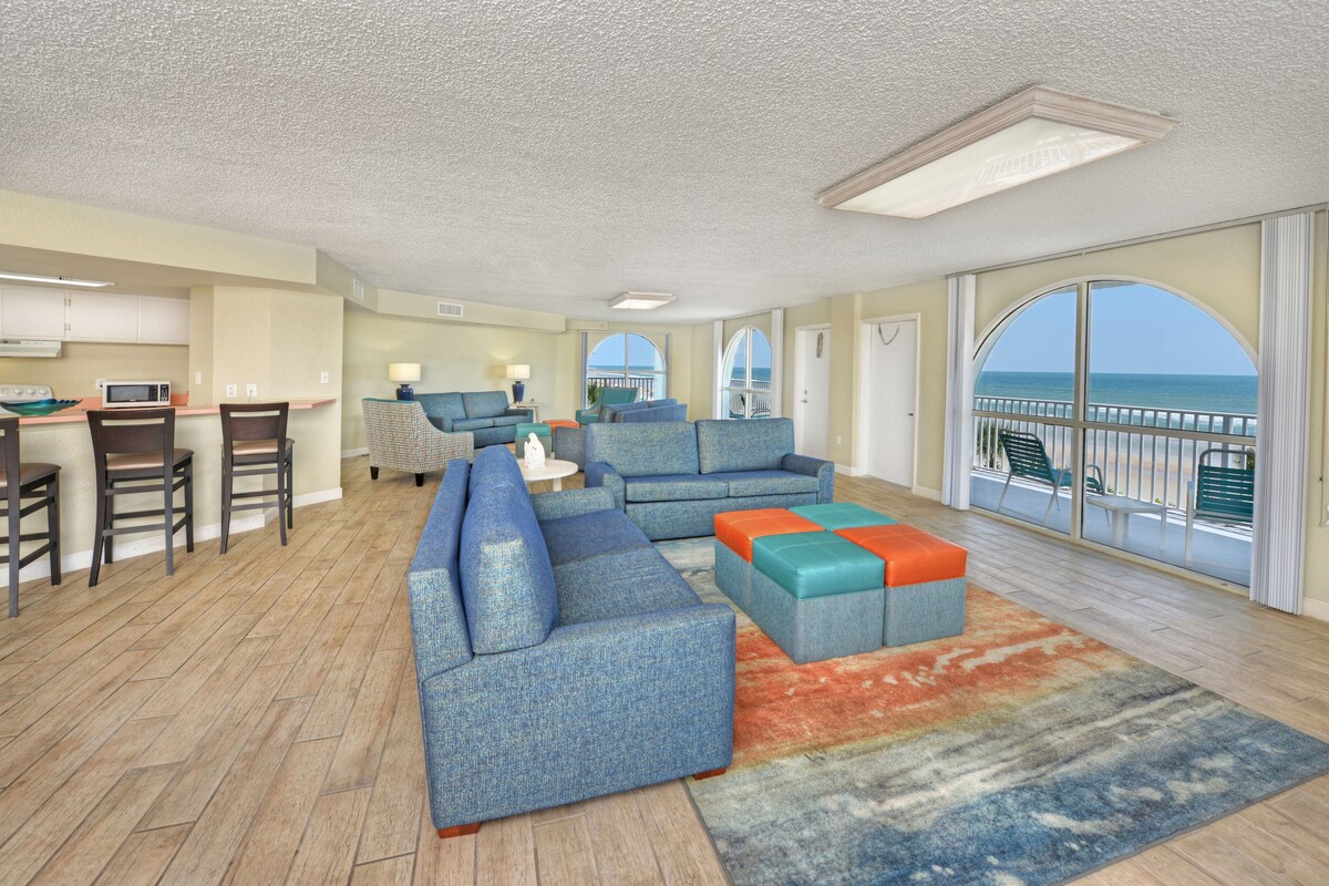 A spacious living area with a large sofa, a coffee table, and a view of the ocean through a balcony.