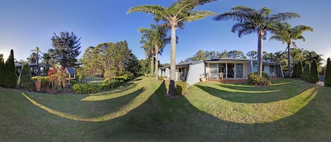 A house with a well-maintained lawn, palm trees, and a small patio area.