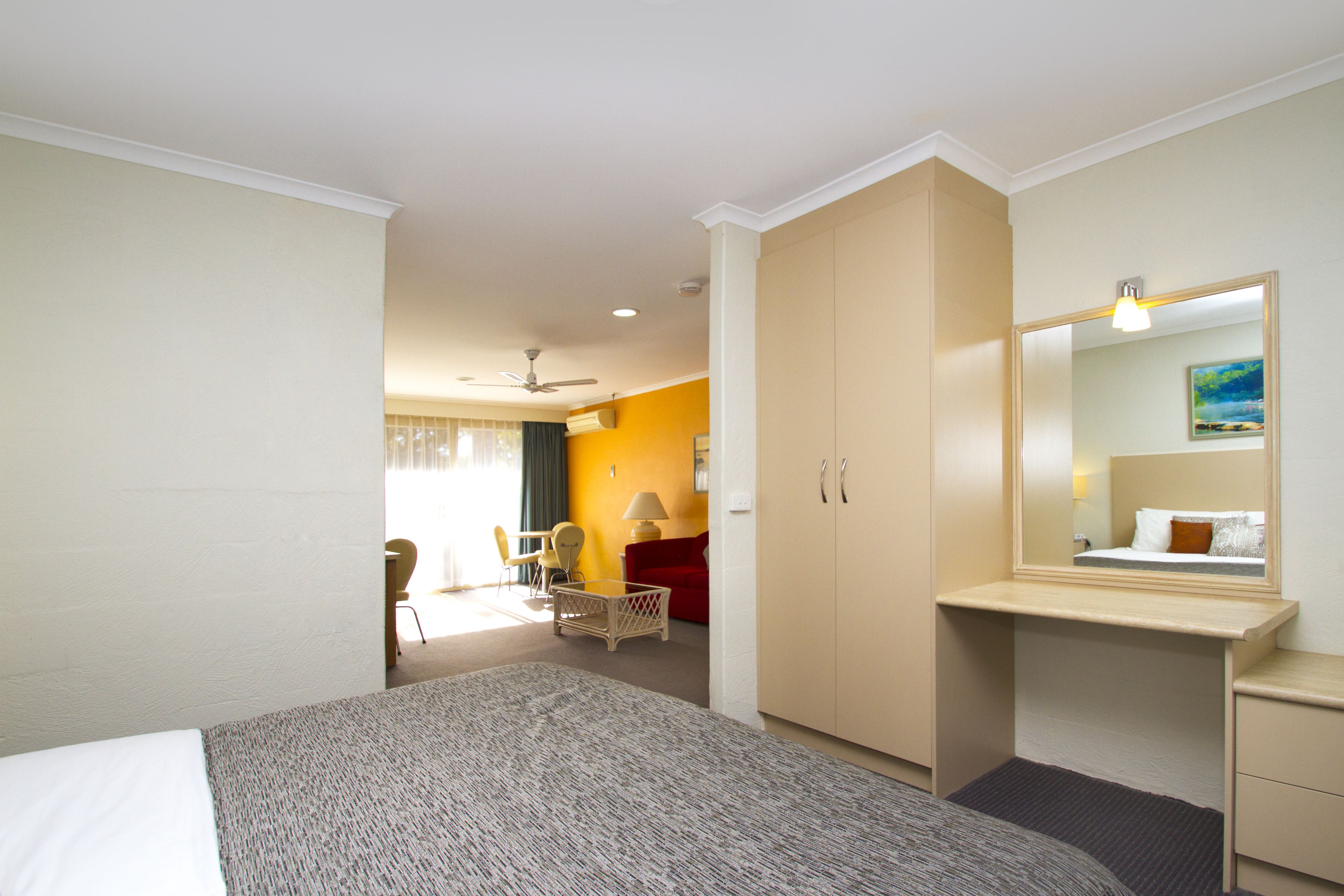 A hotel room with a bed, a desk, a chair, a wardrobe, and a mirror.