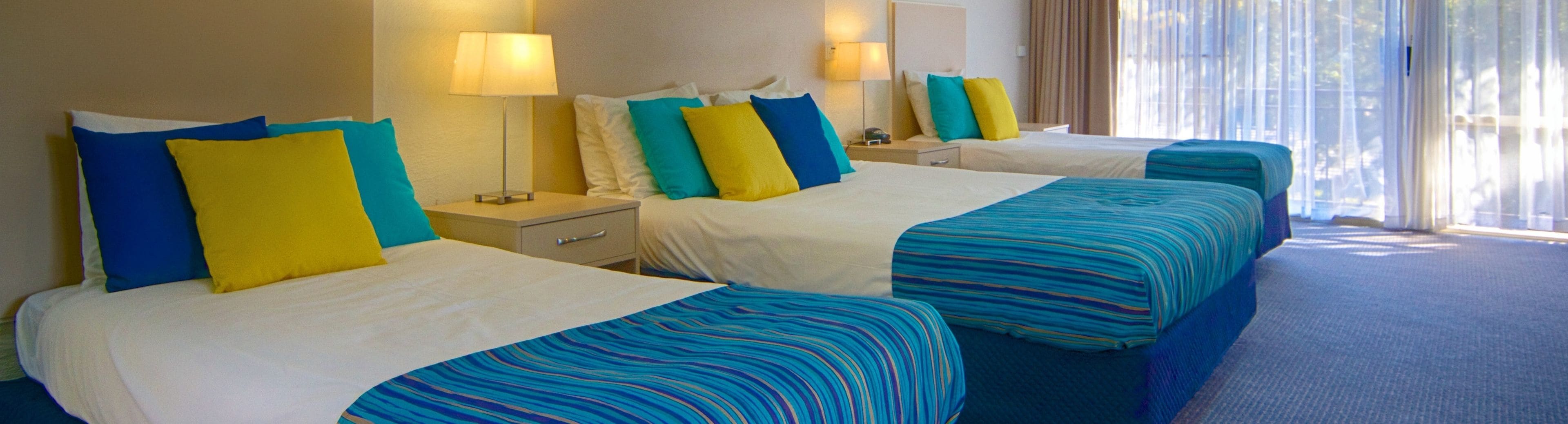 A hotel room with two beds, each with a striped blue and white bedspread, and a nightstand with a lamp.