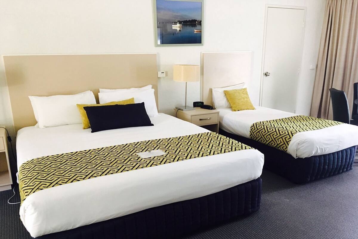 A hotel room with two beds, a nightstand, a lamp, and a view of the sea.
