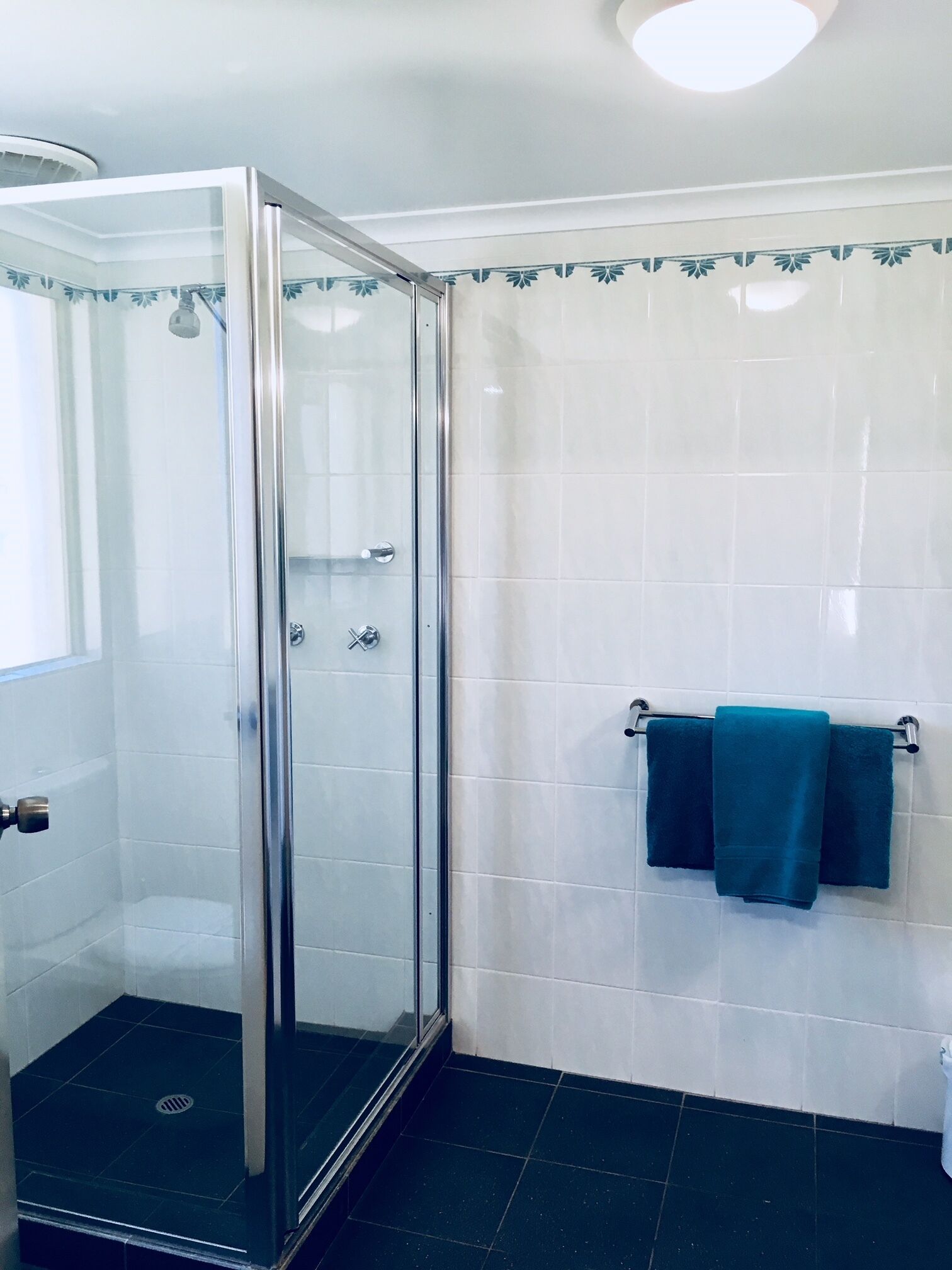 A bathroom with a glass shower enclosure, white tiled walls, and a black tiled floor.
