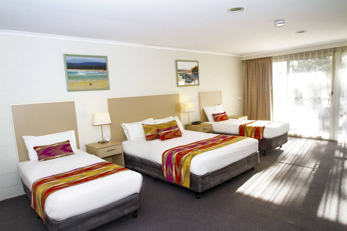A hotel room with three beds, a large window with curtains, and artwork on the walls.