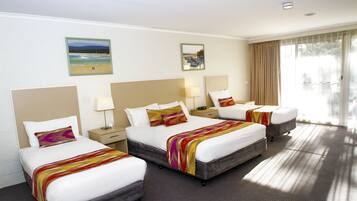 A hotel room with three beds, a large window with curtains, and artwork on the walls.