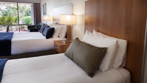 A hotel room with two beds, each with white linens and multiple pillows. There are bedside tables with lamps and a view of greenery outside. - Fairway Motor Inn (Pambula)