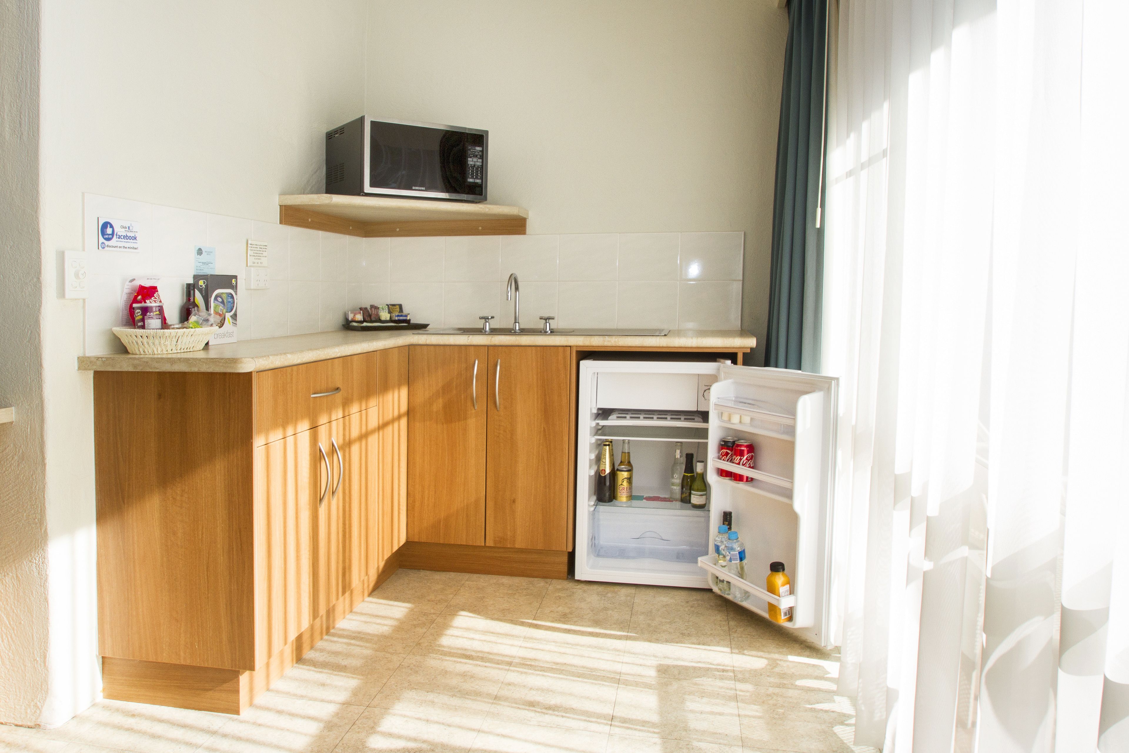 Una cocina funcional con armarios de madera, microondas, refrigerador y pileta.