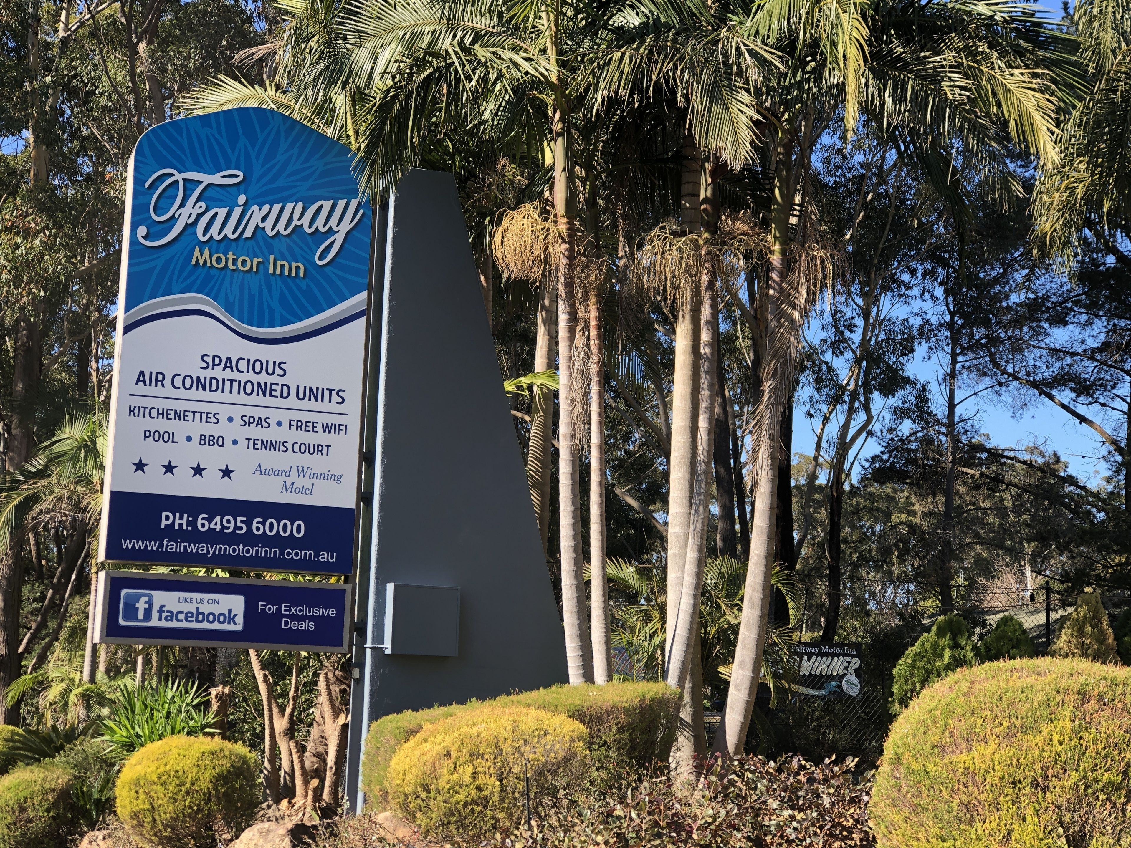 A sign for the Fairway Motor Inn highlighting amenities like spacious air-conditioned units, kitchens, spas, free WiFi, pool, BBQ, and a tennis court.