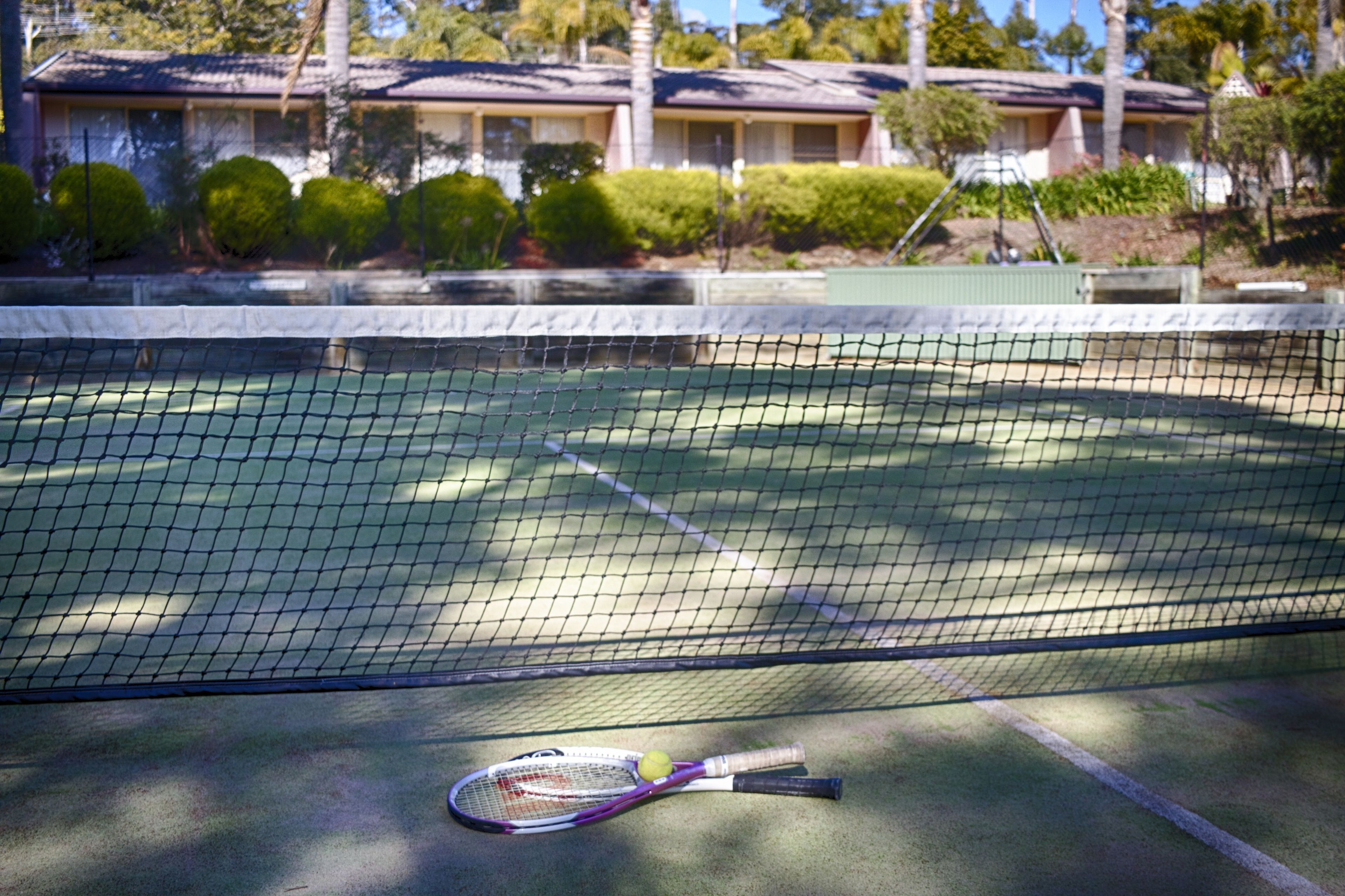 En tennisbana med nät, ett tennisracket och en boll.