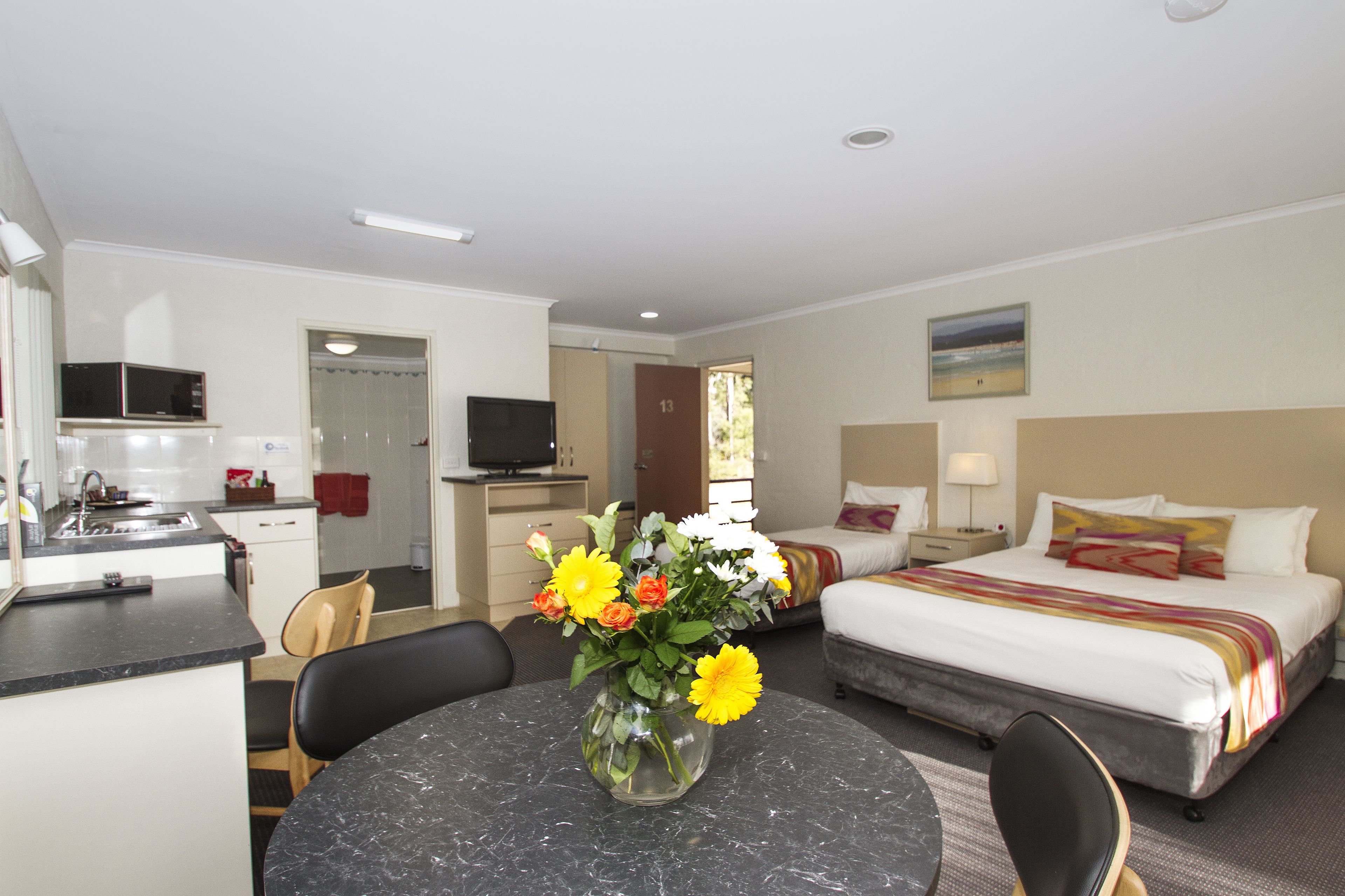 A hotel room with a bed, a desk with a computer, a dining area with a table and chairs, and a kitchen area.