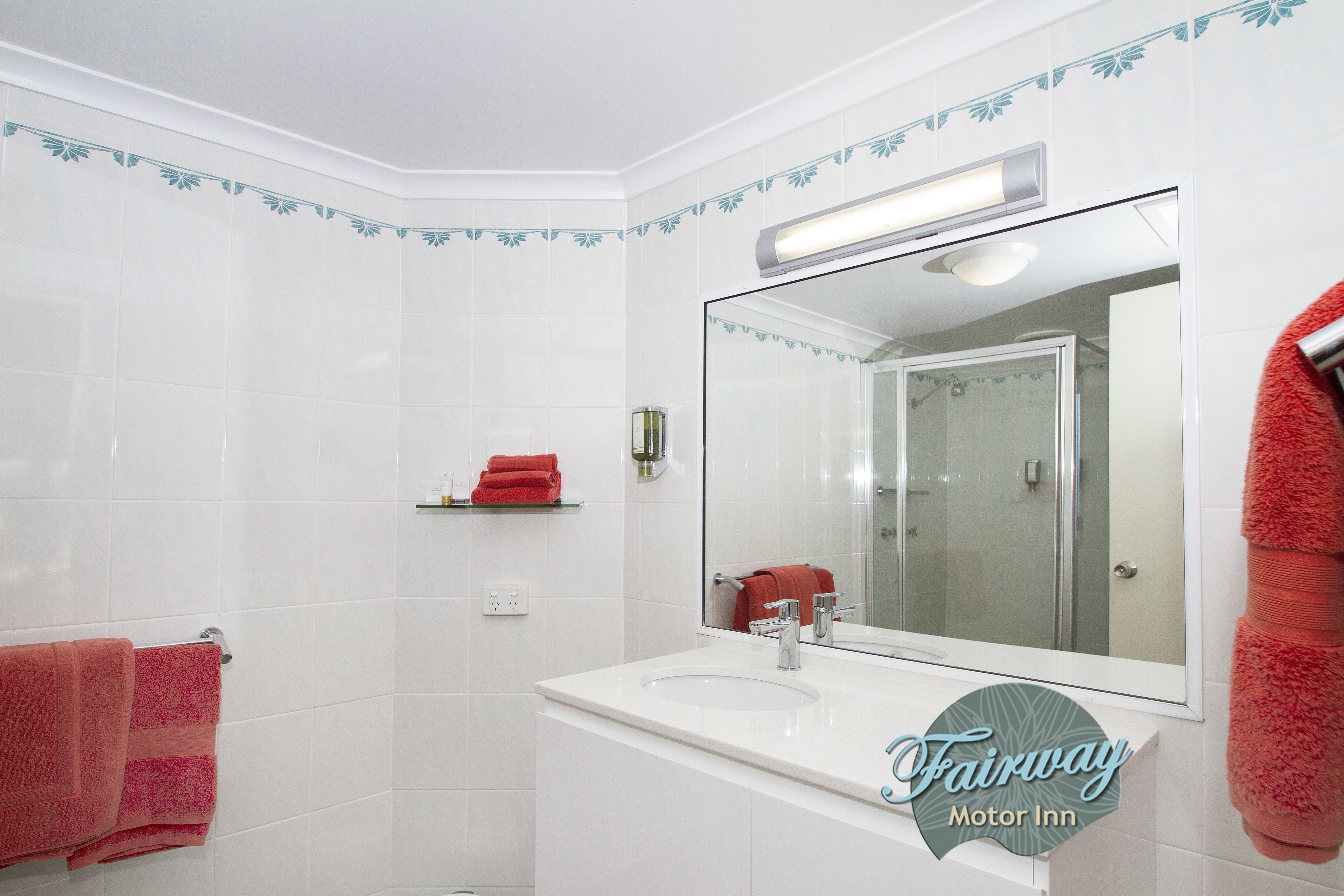 Un baño con azulejos blancos, un espejo grande, un lavamanos y dos toallas rojas.