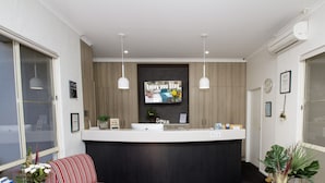 A reception area with a counter, two pendant lights, a wall-mounted TV, and framed certificates. - Fairway Motor Inn (Pambula)