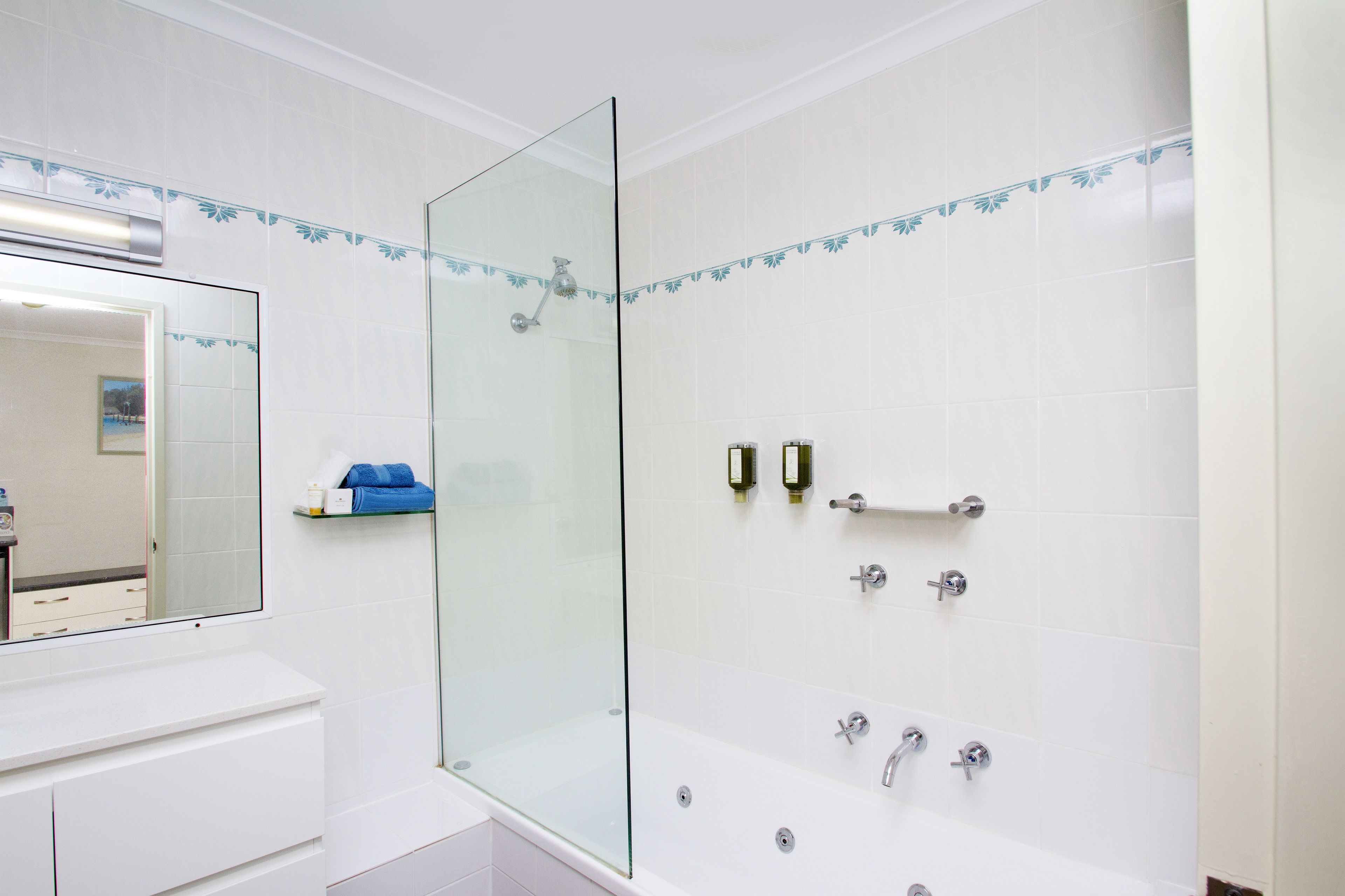 Un baño moderno con cabina de ducha de vidrio, azulejos blancos y un tocador blanco con espejo.