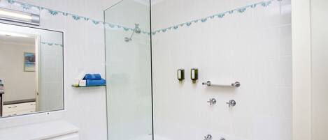 Un baño moderno con cabina de ducha de vidrio, azulejos blancos y un tocador blanco con espejo.