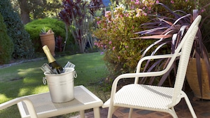 A patio with a white wicker chair and a metal table holding a bottle of champagne. - Fairway Motor Inn (Pambula)