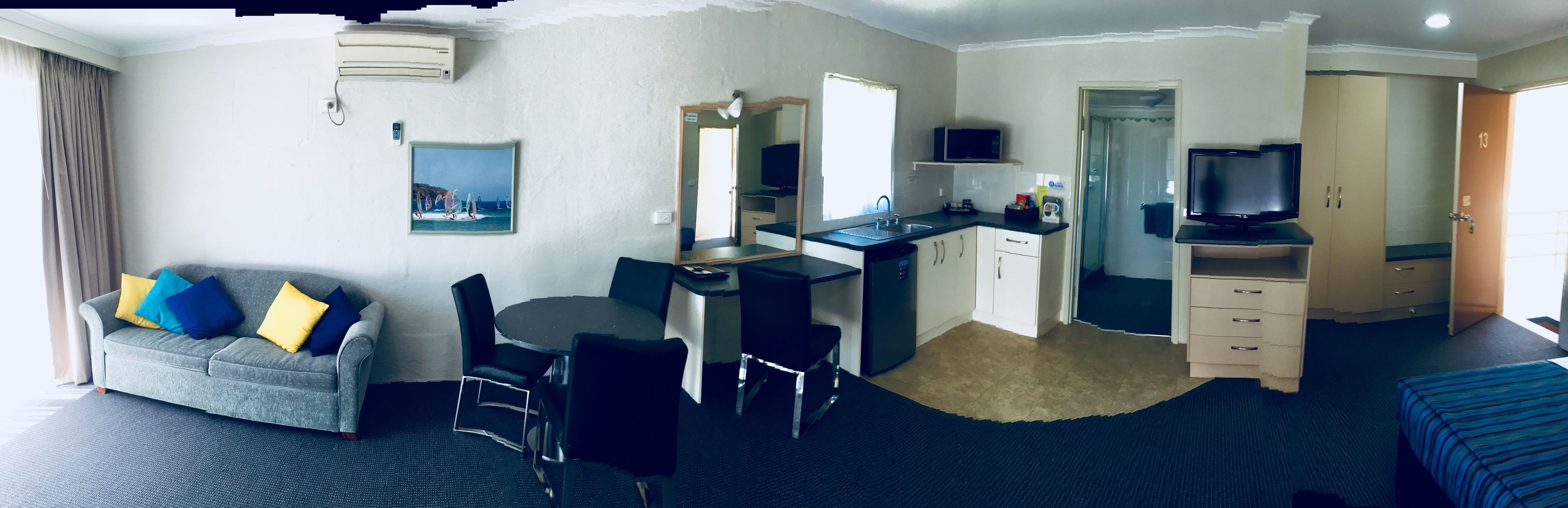 Een hotelkamer met een bank, eettafel, stoelen, een kitchenette, een televisie en een bed.