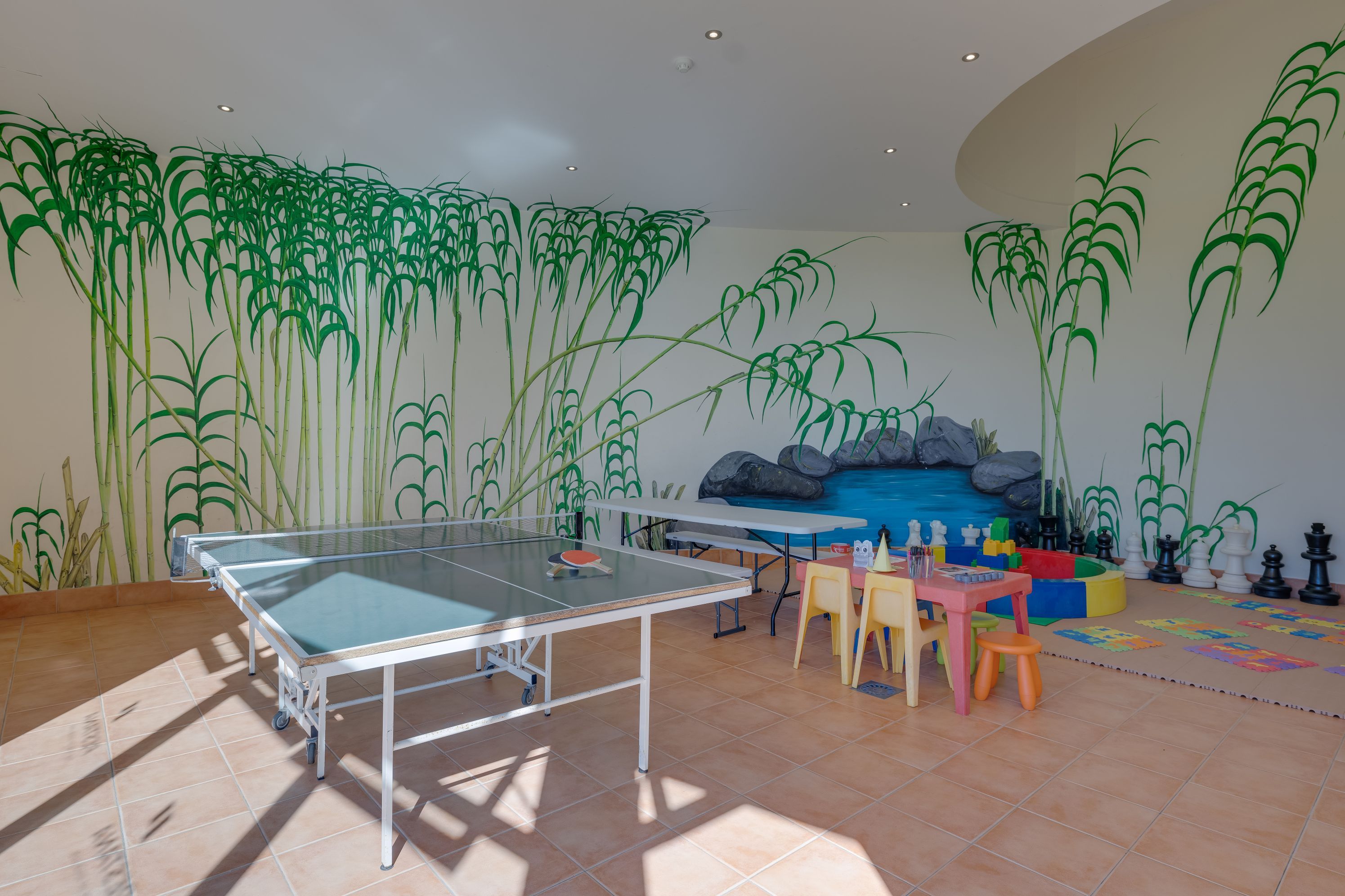 A room with a ping pong table, chairs, and a wall mural.
