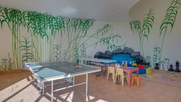 A room with a ping pong table, chairs, and a wall mural.