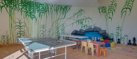 Une pièce équipée d’une table de ping-pong, de chaises et d’une fresque murale.