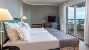 A hotel room with a bed, two bedside lamps, a television, a desk, and a view of the balcony.