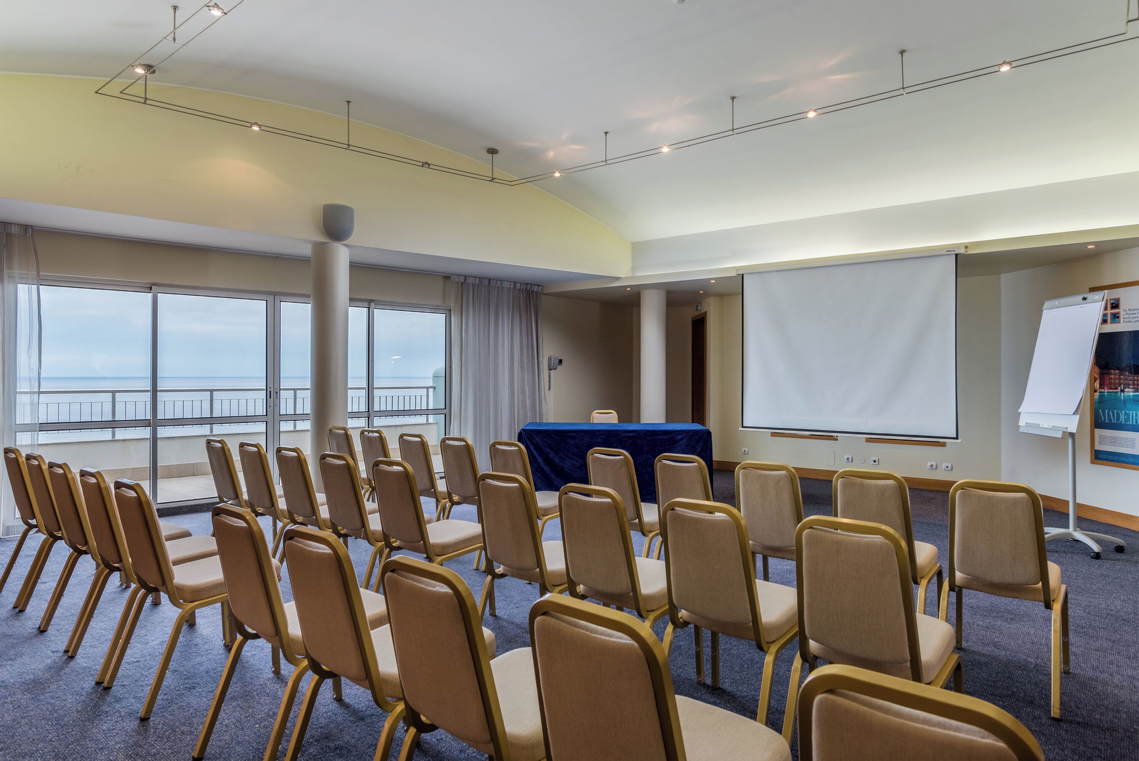 Ein Konferenzraum mit Reihen von Stühlen, einer Projektionsleinwand und einer Präsentationswand.