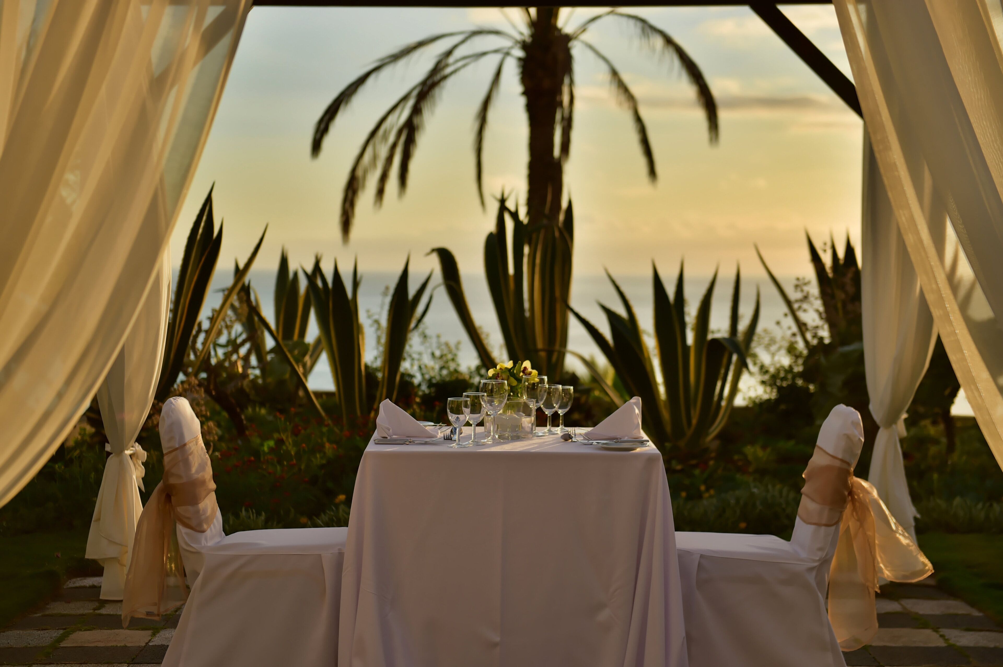 Mesa lista para dos, con vista a palmeras y un atardecer.