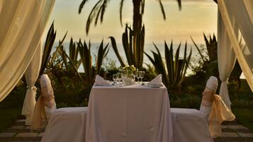Mesa lista para dos, con vista a palmeras y un atardecer.