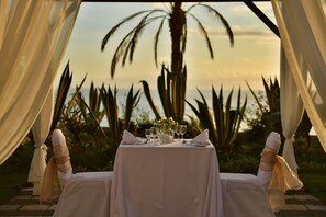Mesa lista para dos, con vista a palmeras y un atardecer.