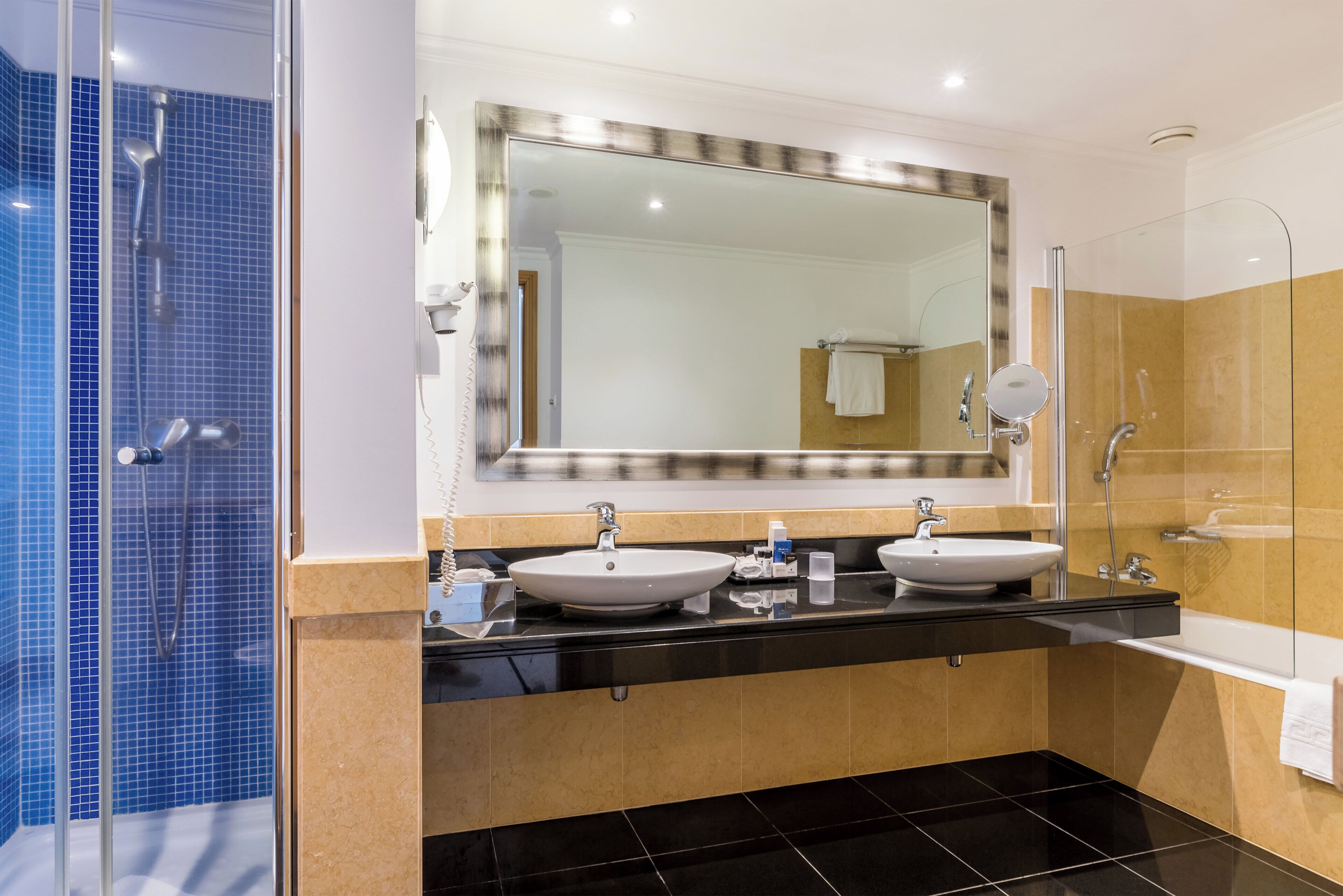 A modern bathroom with two sinks, a large mirror, and a shower area.