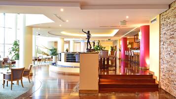 A hotel lobby with a central reception desk, seating area, and a staircase leading to upper floors.