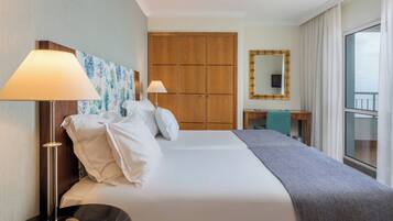Habitación de hotel con cama, dos lámparas de noche, un armario de madera, un escritorio con espejo y vistas por la ventana.
