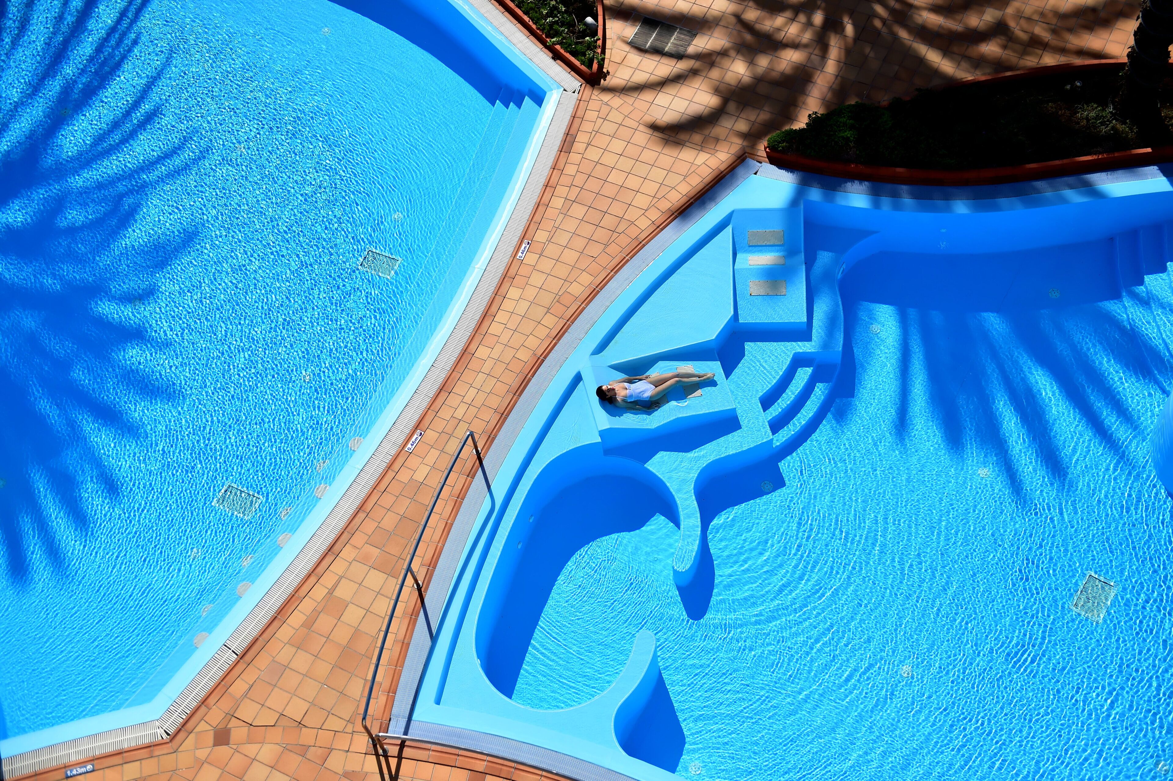 A large swimming pool with a diving board and a slide, surrounded by a tiled deck.