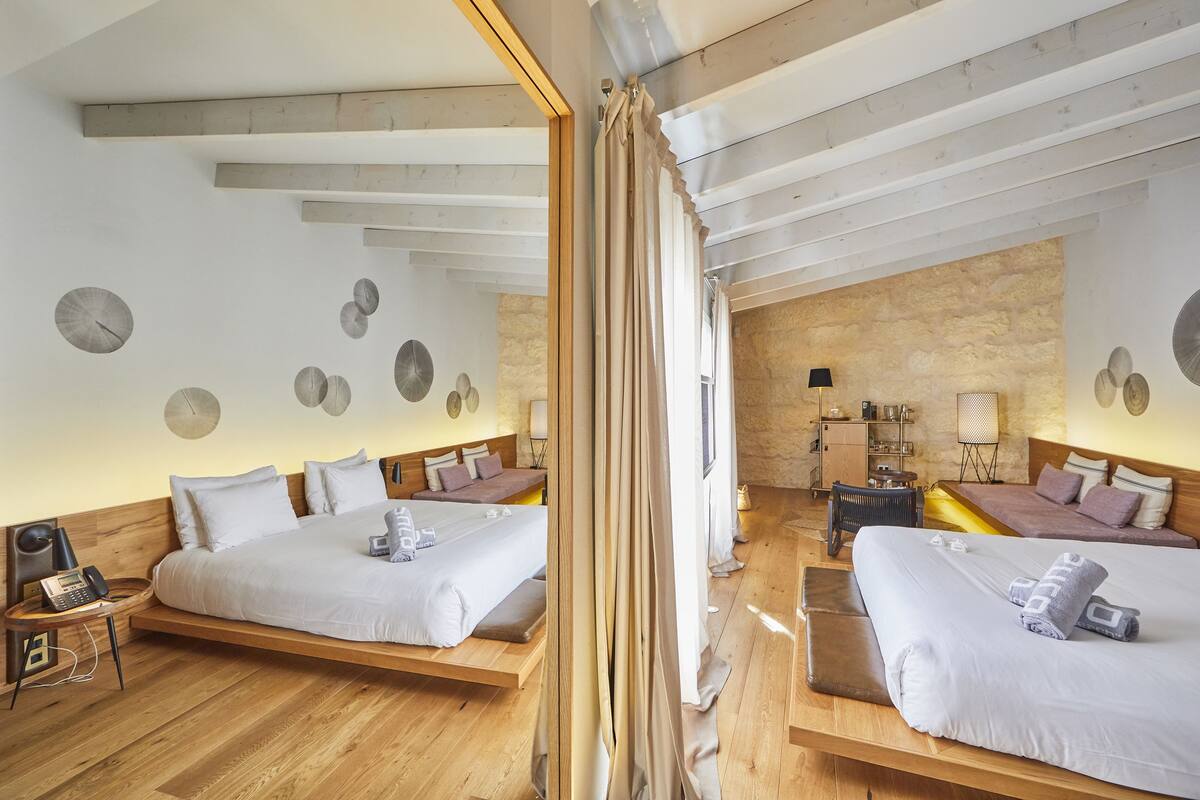 Een moderne hotelkamer met twee bedden, een houten vloer, een stenen muur en een spiegel die de kamer weerspiegelt.