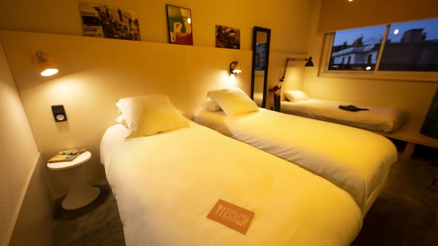 A hotel room with two beds, a small bedside table, a nightstand, and a window with a view of the city at dusk. - Artyster Clermont-Ferrand (Clermont-Ferrand)