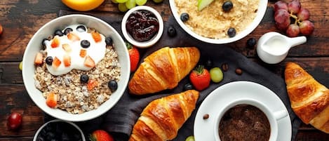 A breakfast setting with bowls of oatmeal, yogurt, and granola, alongside croissants, grapes, strawberries, and coffee.