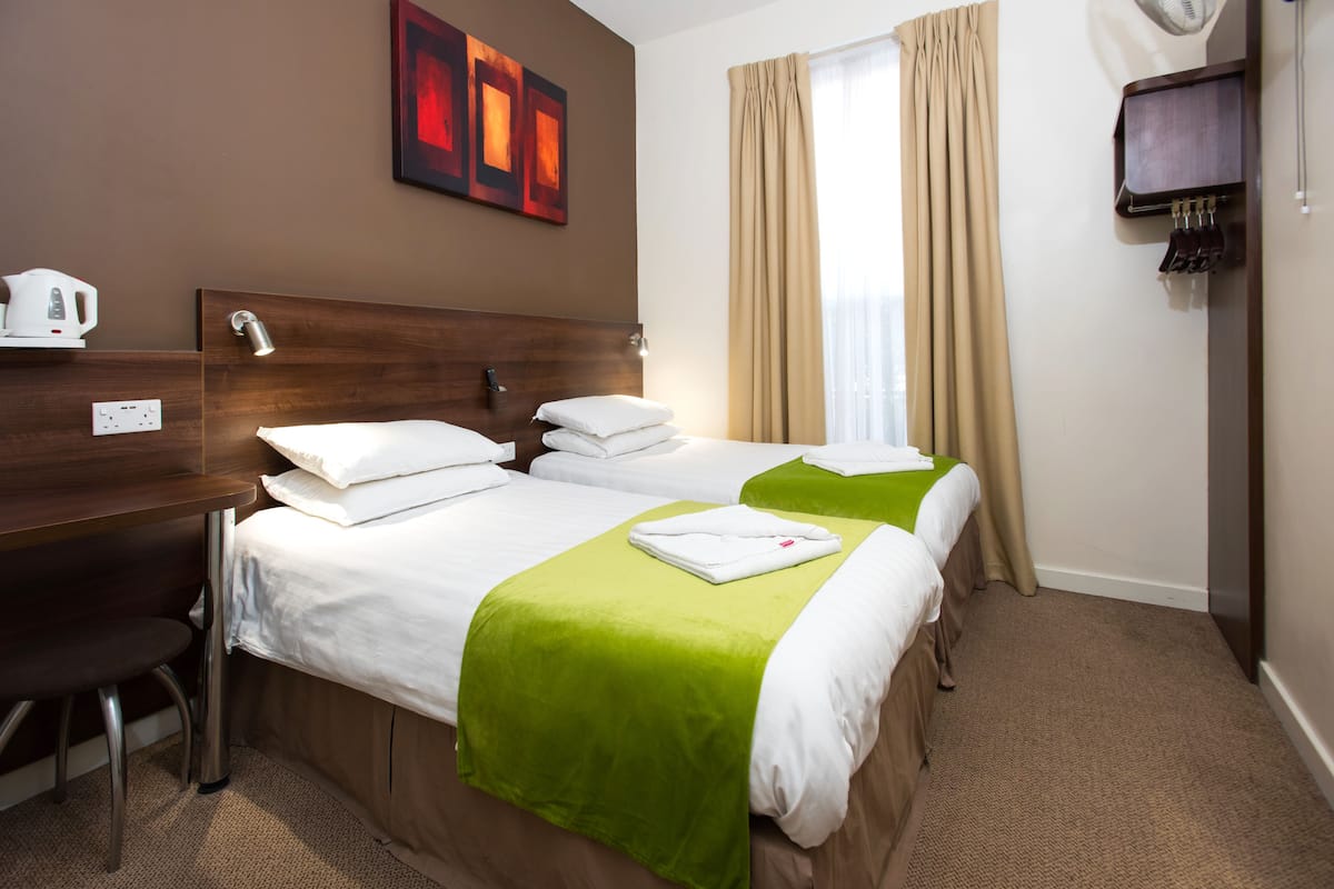 A hotel room with two beds, a desk, a chair, a television, and a painting on the wall.