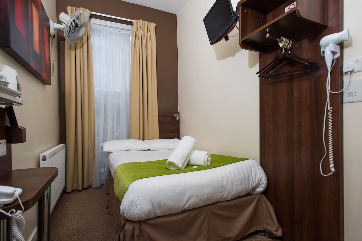 A hotel room with a bed, a desk with a phone, a hairdryer, a mirror, and a TV mounted on the wall.