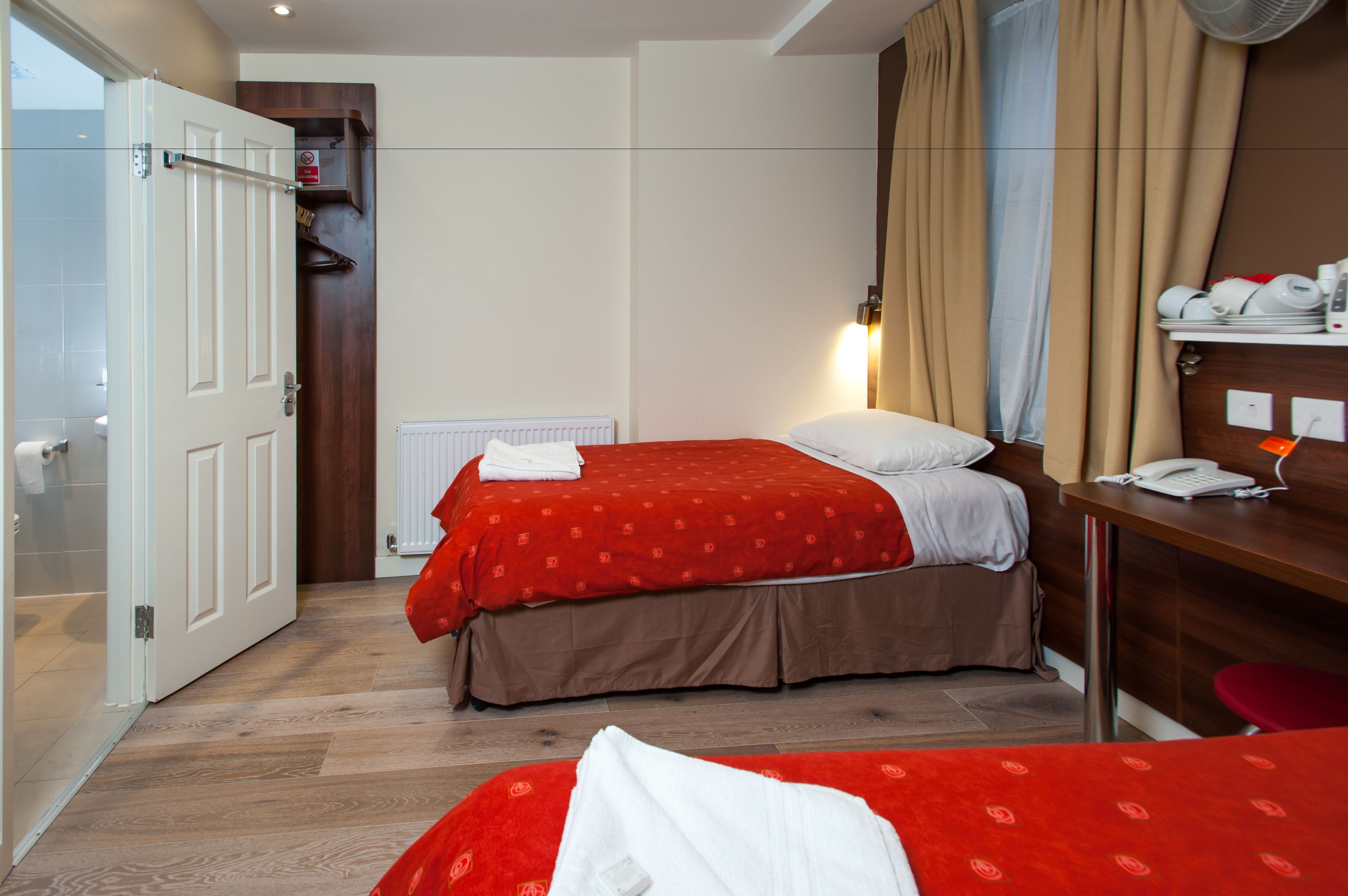 A hotel room with a bed, a desk with a telephone, a radiator, and a door leading to a bathroom.