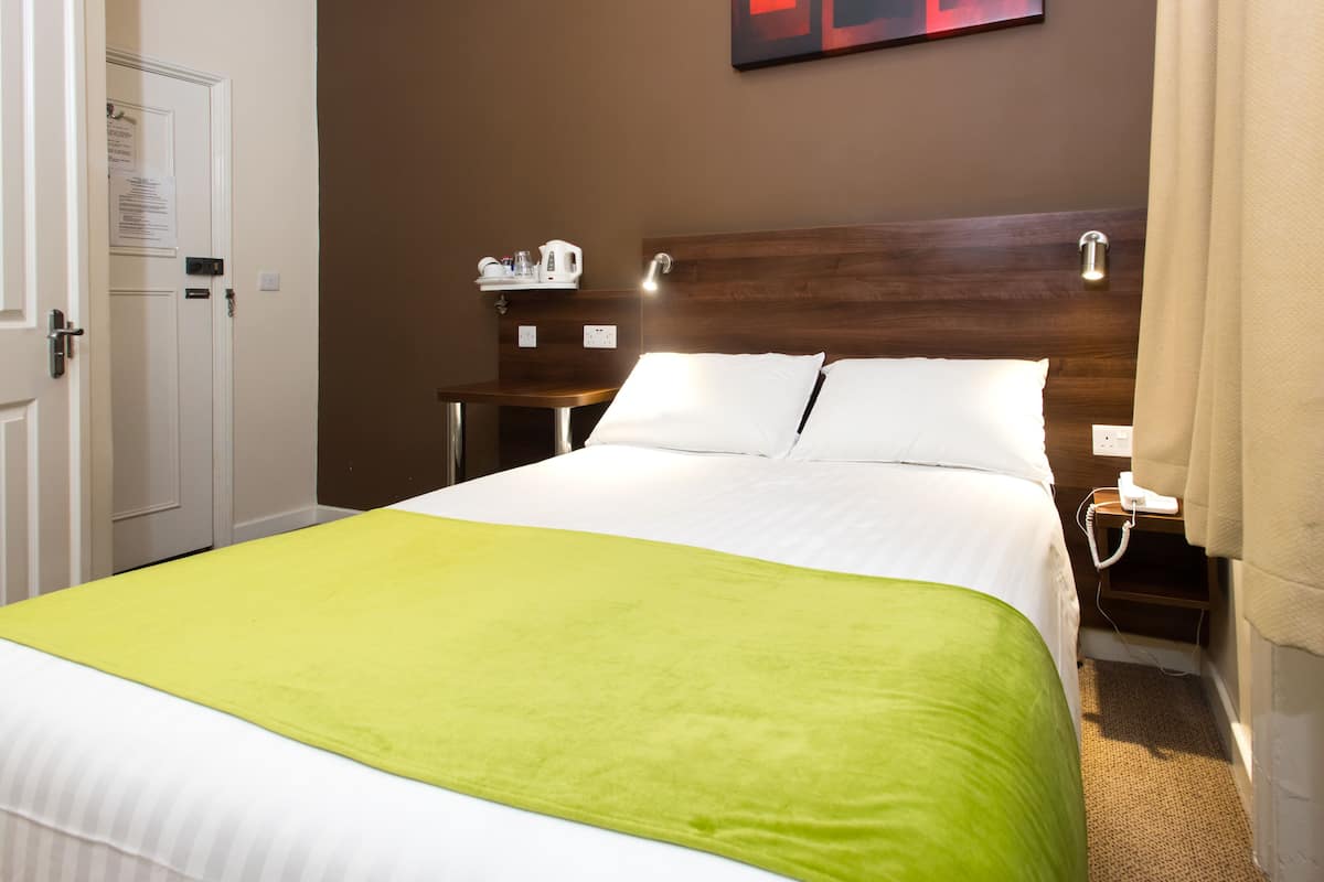 A hotel room with a bed, a nightstand, a lamp, and a door.